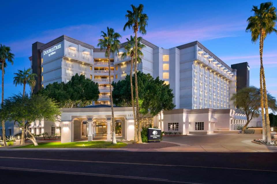 Double Tree hotel exterior at dusk with palm trees, illuminated entrance, and multi-story building