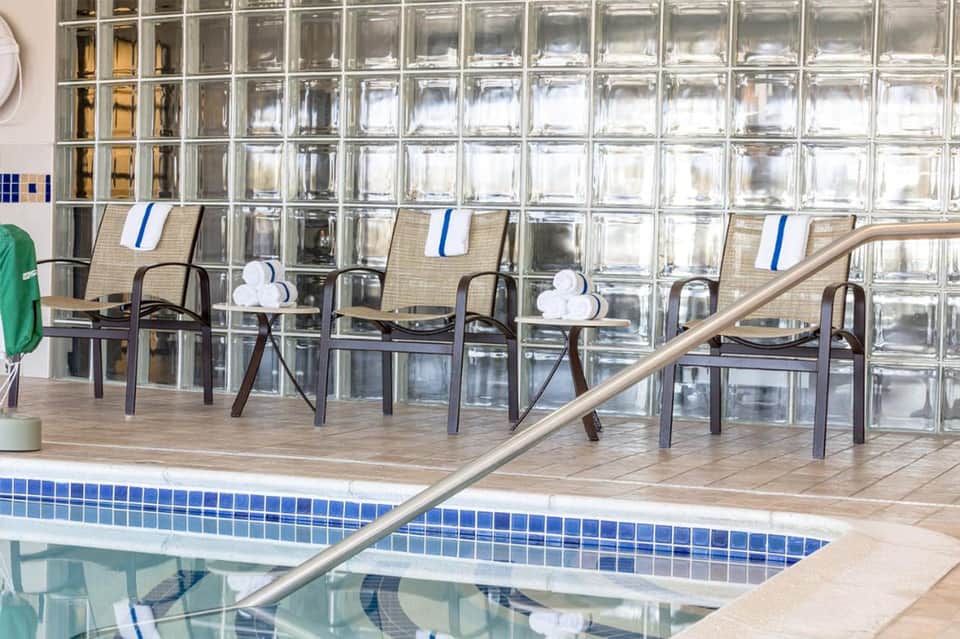 Indoor pool area with glass block wall, lounge chairs with blue cushions, and wooden deck