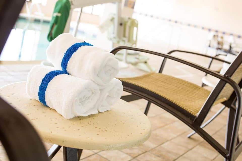 Two rolled white towels with blue stripes on a beige poolside table next to lounge chairs