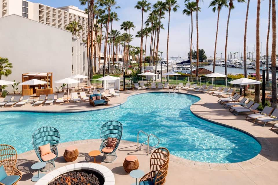 Waterfront resort pool with palm trees, lounge chairs, umbrellas, and marina views in background