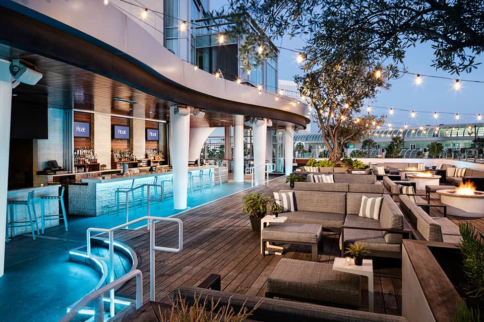 Rooftop bar and lounge with blue-lit pool, outdoor seating, string lights, and glass greenhouse structures