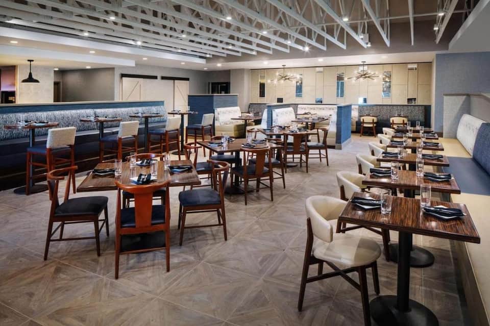 Contemporary restaurant dining area with mid-century wooden furniture, blue accent seating, and geometric ceiling
