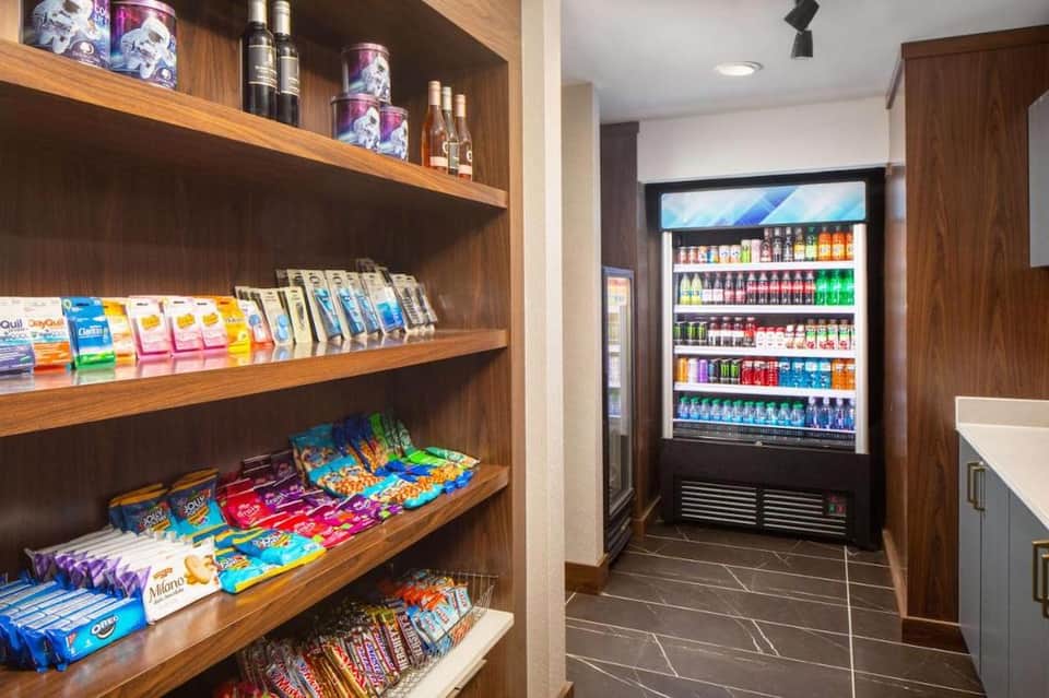 Hotel convenience store with wooden shelves stocked with snacks and refrigerated beverage display