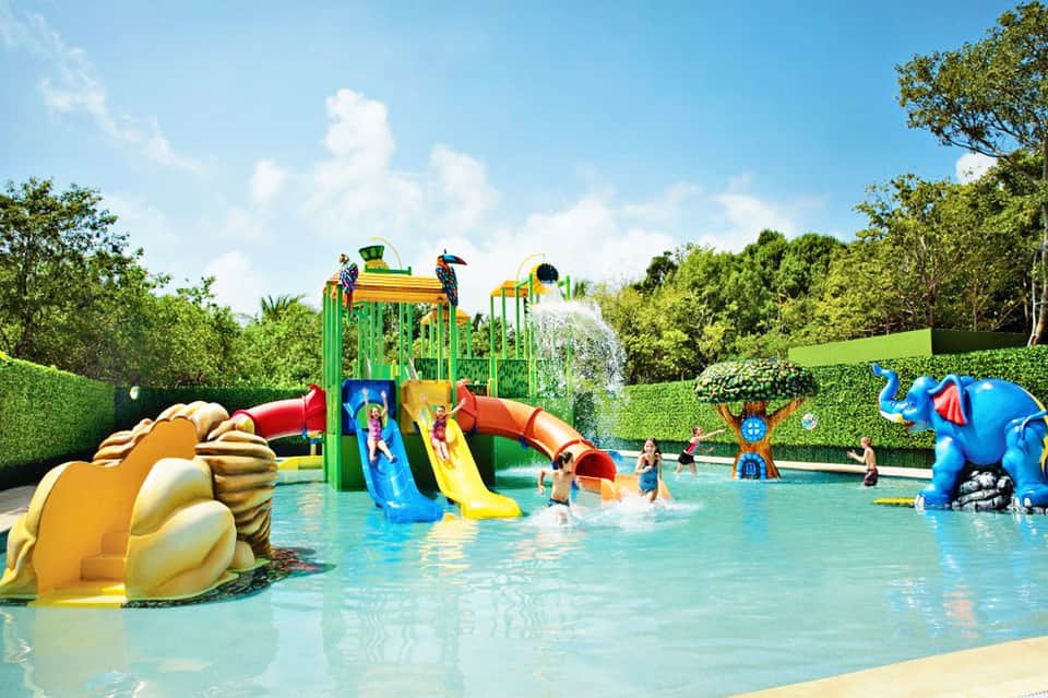Colorful children's water park with splash pad, slide structures, and families enjoying shallow pool