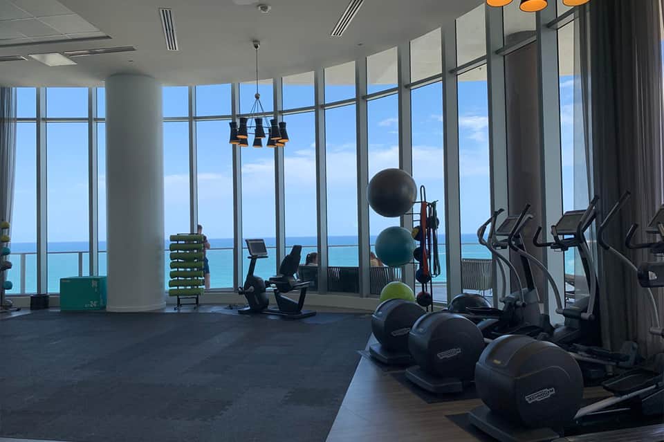 Modern fitness center with floor-to-ceiling windows, exercise equipment, and ocean views