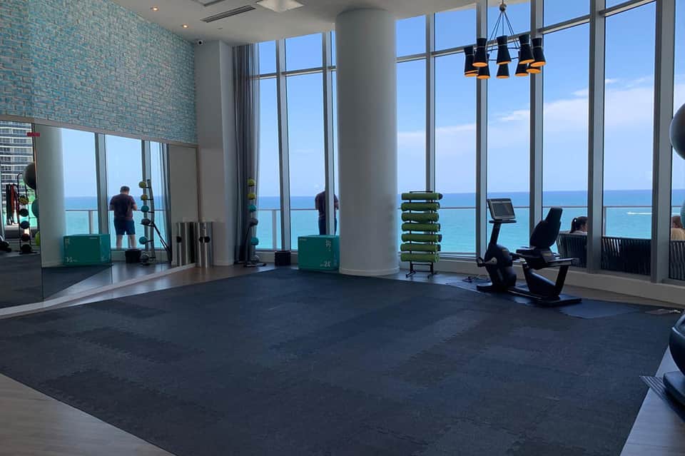 Fitness center with ocean view windows, exercise equipment, and mirrors overlooking turquoise water