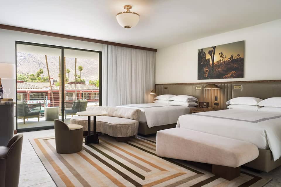 Spacious hotel bedroom with two queen beds, balcony access, and contemporary furnishings