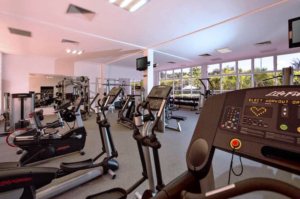 Fitness center with cardio equipment, treadmills, and floor-to-ceiling windows overlooking palm trees