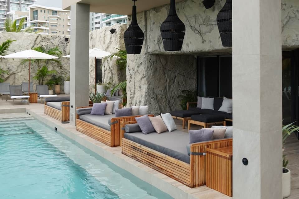 Contemporary pool area with wooden lounge beds, stone walls, and modern architectural design