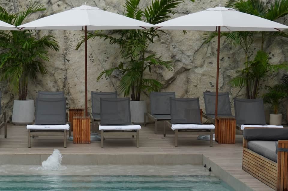 Poolside lounge area with gray chaise lounges under white umbrellas and concrete wall backdrop
