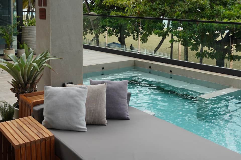 Contemporary pool with turquoise water, concrete lounging area with cushions, and city view