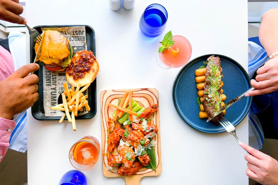 Overhead view of gourmet dishes and colorful cocktails on white table during meal service