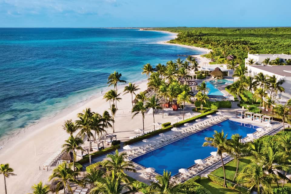 Luxury beachfront resort with multiple pools, palm trees, and pristine white sand beach with turquoise water