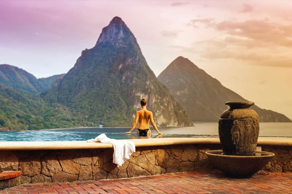 Woman in hot spring pool overlooking dramatic mountain peaks and tropical landscape at golden hour