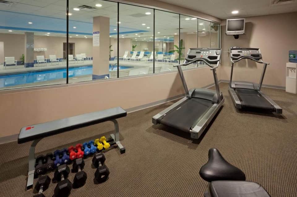 Fitness center with treadmills, dumbbells, and indoor pool visible through glass partition