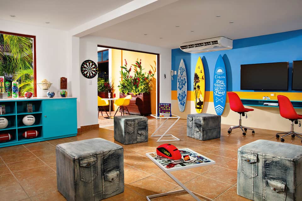 Colorful recreational room with turquoise storage, surfboard wall art, denim ottomans, and flatscreen TVs