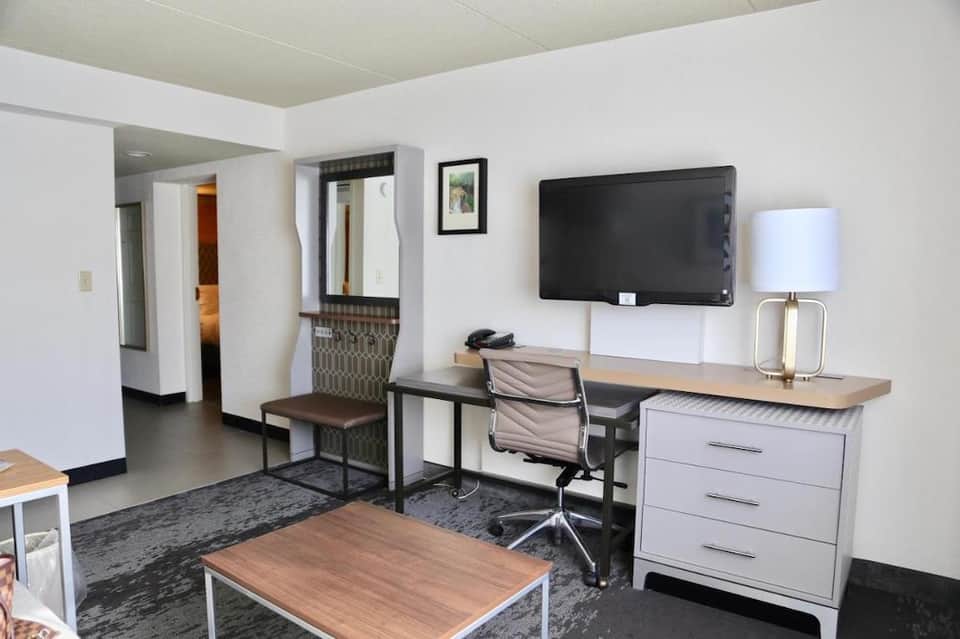 Hotel suite with work desk, TV, comfortable seating, and modern furnishings in neutral tones