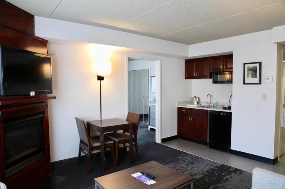 Hotel suite living area with fireplace, kitchenette, dining table, and TV entertainment center
