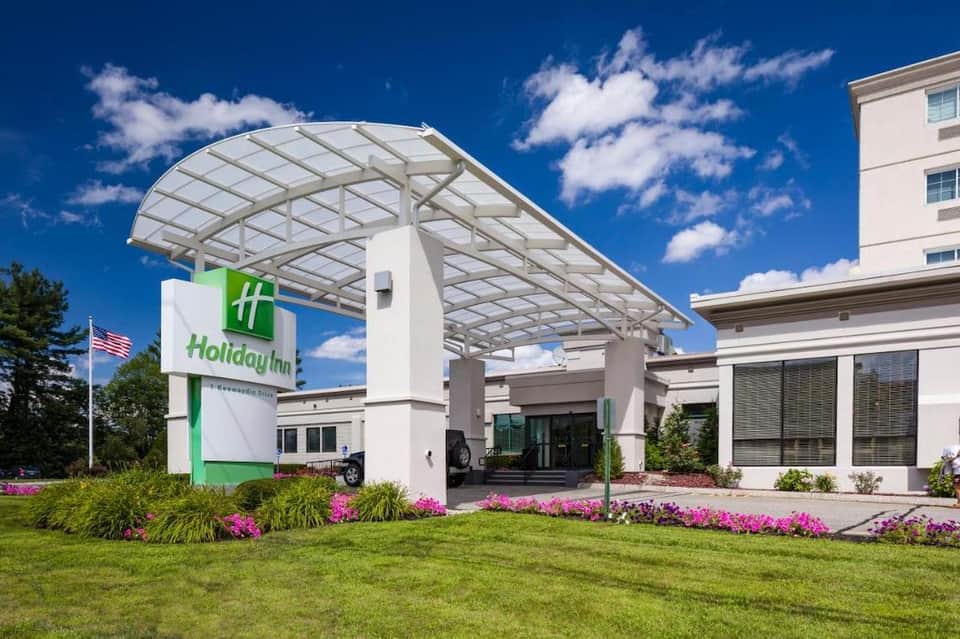 Holiday Inn hotel entrance with green signage, white canopy, and pink flowering landscaping