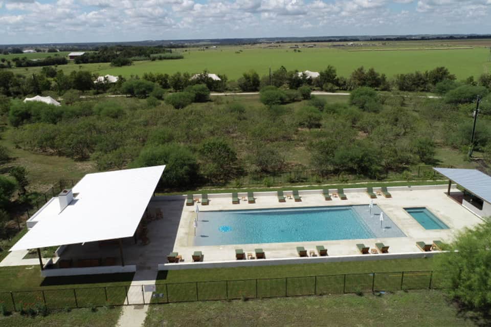 Aerial view of resort pool complex with white shade structure and lounge chairs overlooking rural landscape
