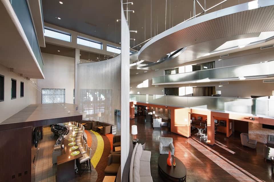 Modern multi-level hotel atrium with curved balconies, dining area, and contemporary architectural design