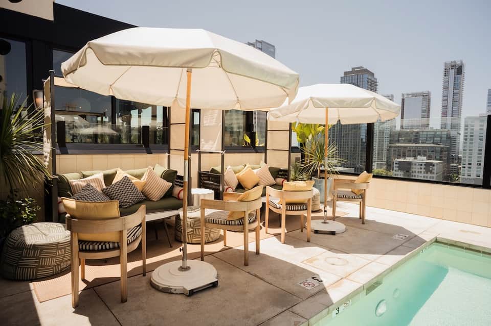 Rooftop terrace with lounge seating, umbrellas, and small pool overlooking city skyline