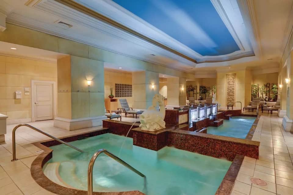 Luxury spa indoor pool facility with teal water, soaking tubs, and elegant beige stone accents