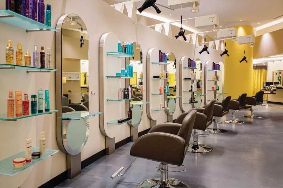 Modern salon interior with mirrored styling stations, teal shelving, and professional hair dryers