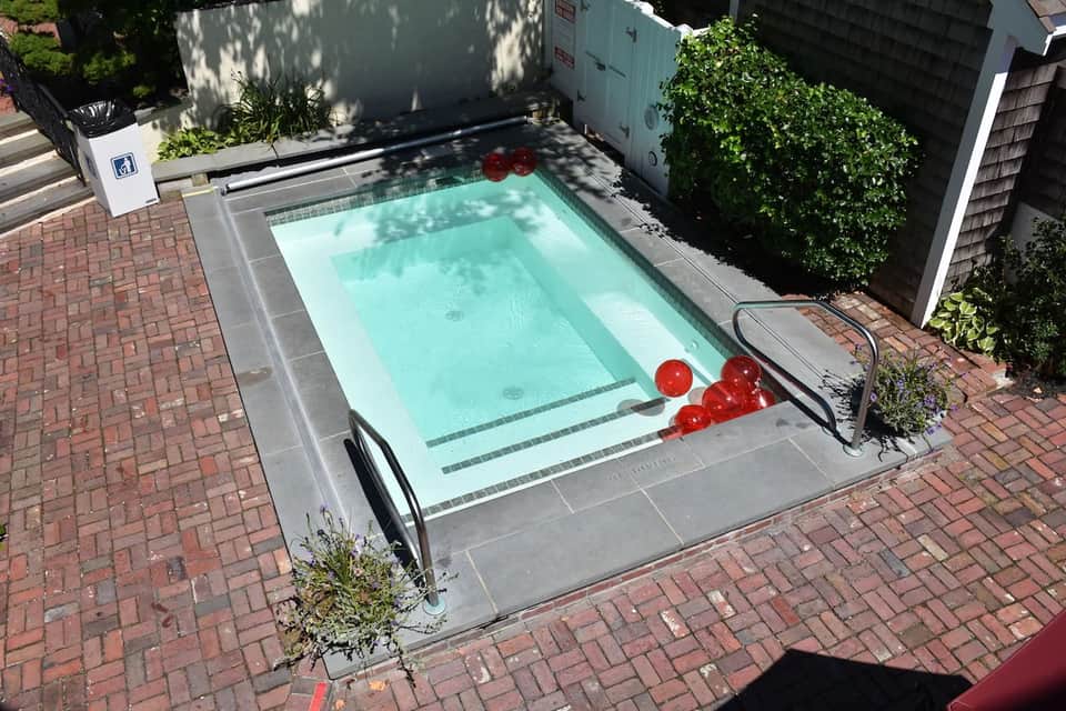 Compact rectangular swimming pool surrounded by brick patio and ivy-covered walls