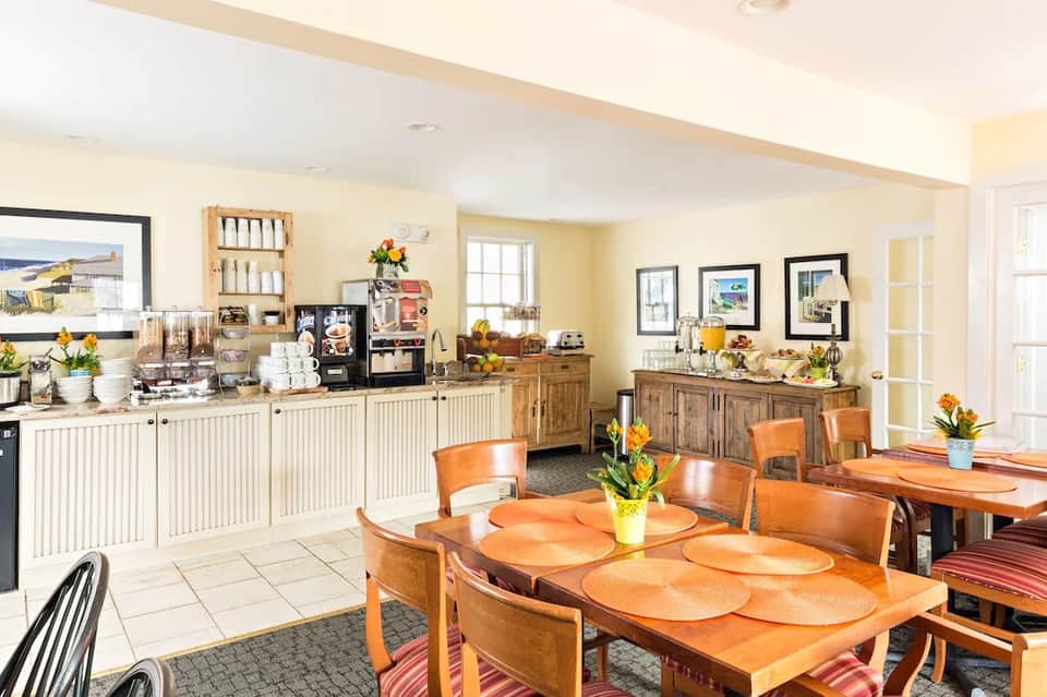 Bright hotel kitchen and dining area with wooden cabinets, dining table, and coastal artwork