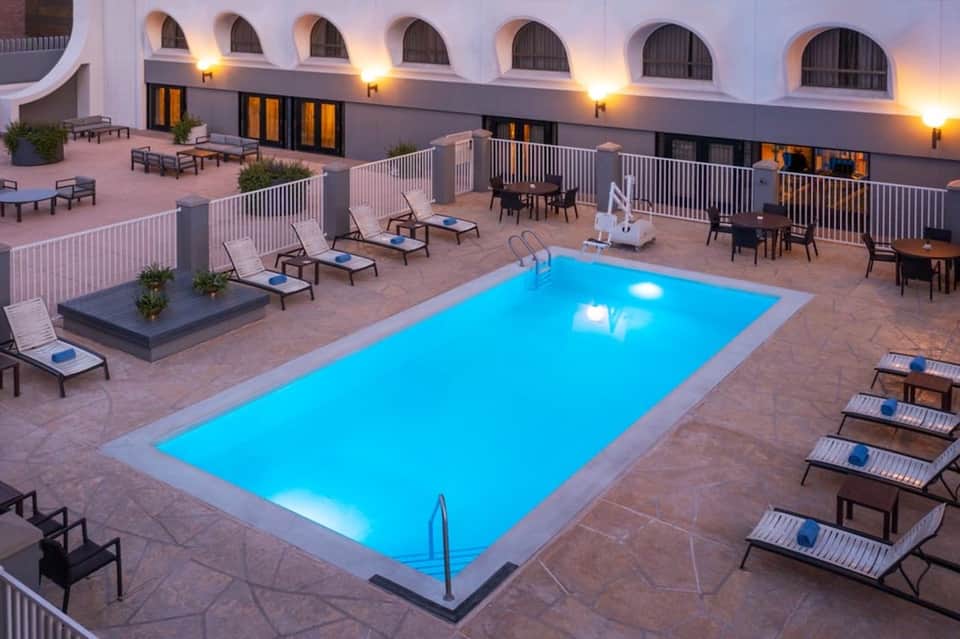 Illuminated resort pool deck at dusk with lounge chairs, white railings, and arched windows of the main building