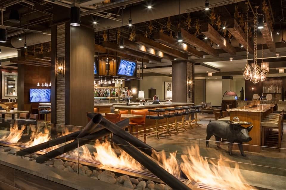 Upscale lounge with fireplace, bar seating, and modern wood ceiling design