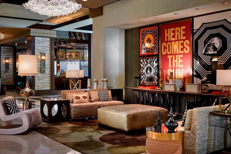 Modern hotel lobby lounge with gold and bronze furniture, red neon signage, and decorative art