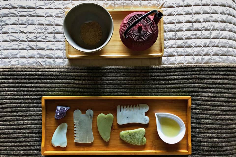 Spa wellness display with jade gua sha tools, teapot, and herbal powder on wooden tray