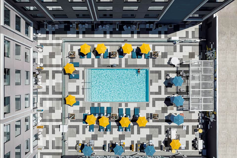 Aerial view of courtyard pool surrounded by yellow umbrellas and lounge seating