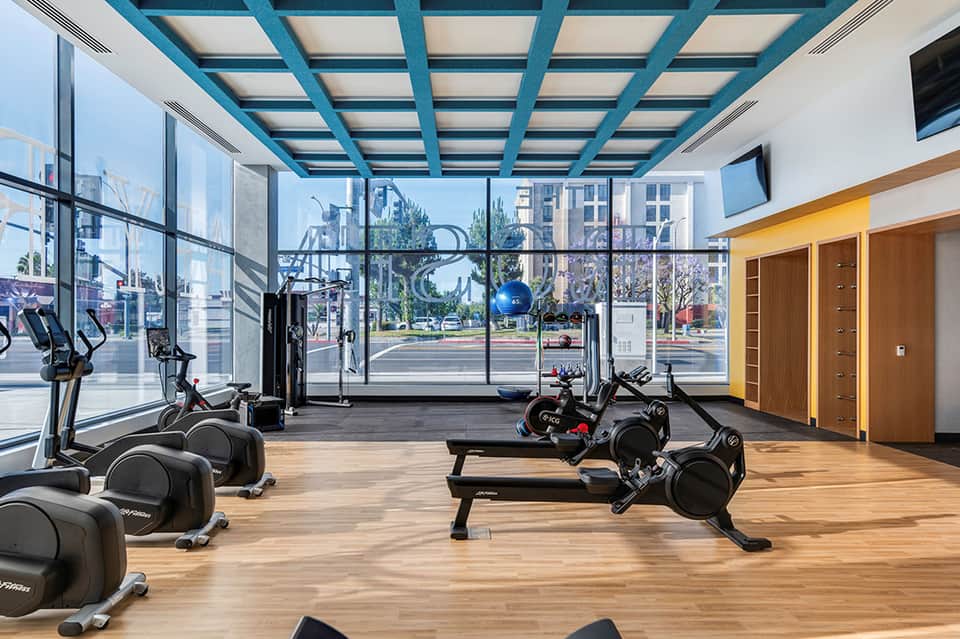 Modern fitness center with cardio equipment and large windows overlooking city street