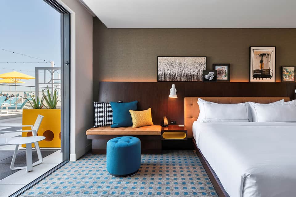 Modern hotel room with orange headboard, blue ottoman, and ocean-view balcony