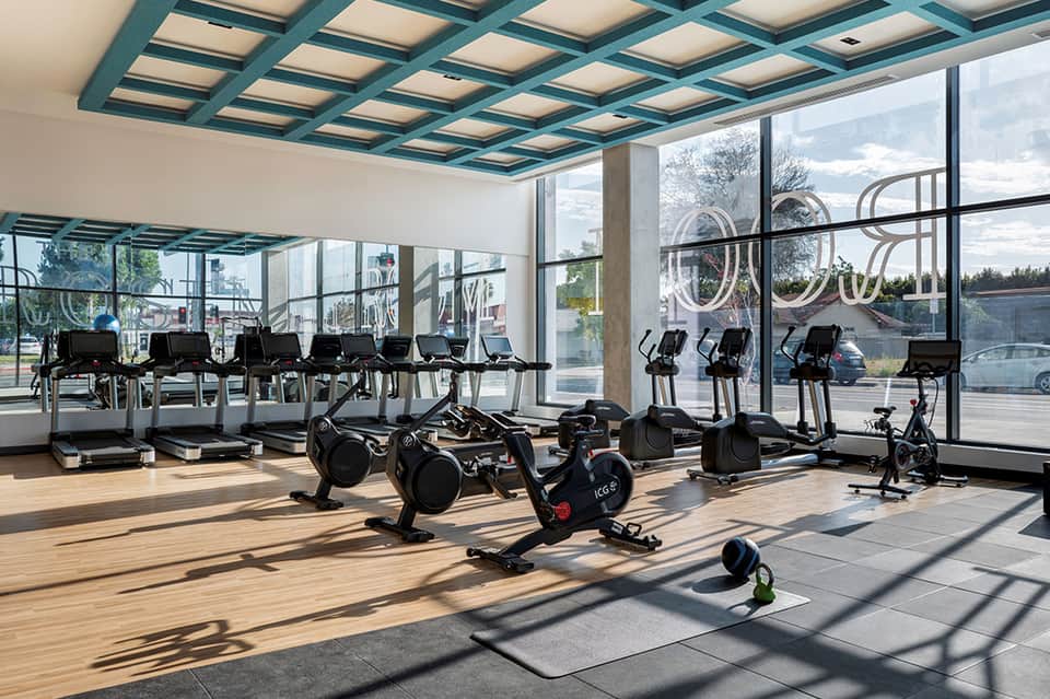 Bright fitness center with exercise bikes, treadmills, and floor-to-ceiling windows with city views