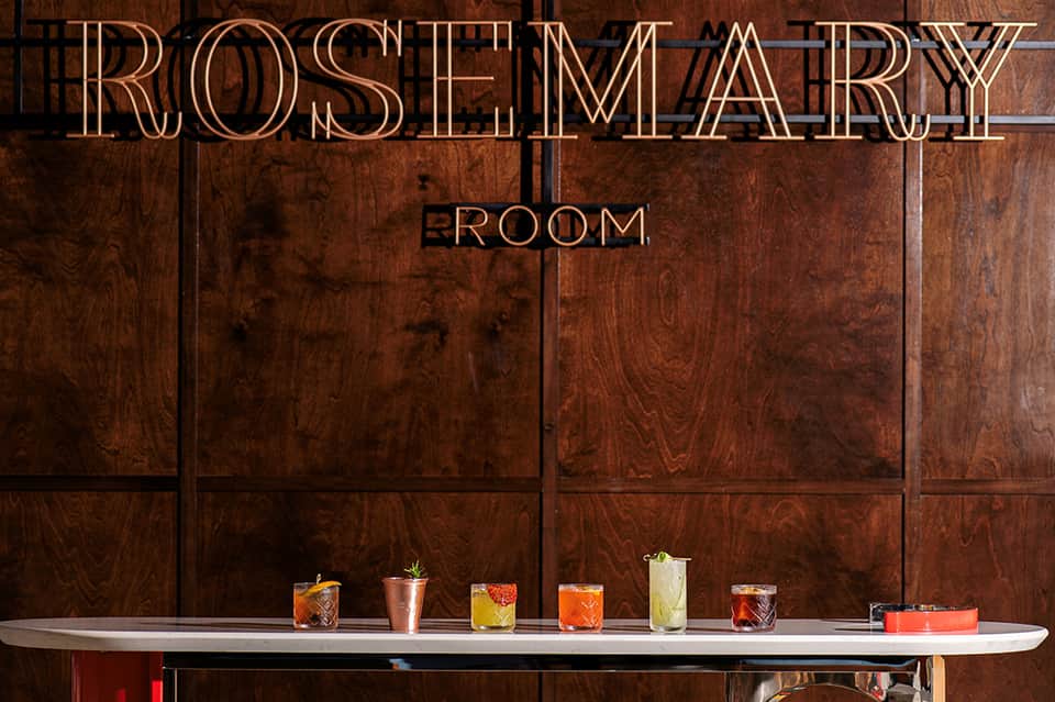 Rosemary Room bar interior with elegant wood paneling and colorful cocktails on counter