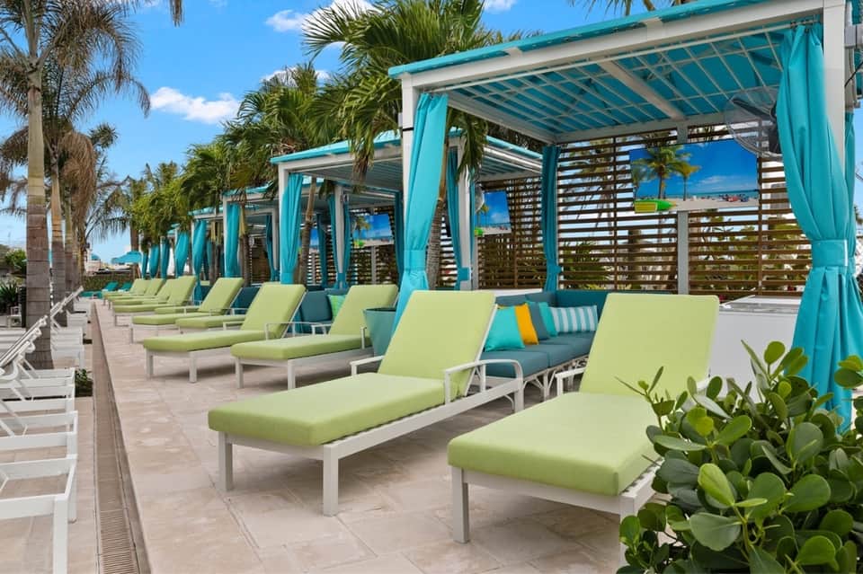 Covered cabana lounge area with lime green loungers, turquoise railings, and palm trees