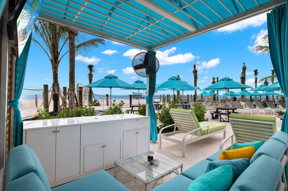 Covered oceanfront lounge area with turquoise pergola, white cabinetry, and beach views