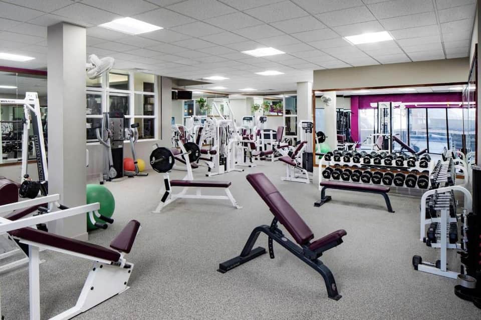 Spacious fitness center with weight machines, dumbbells, exercise benches, and large windows