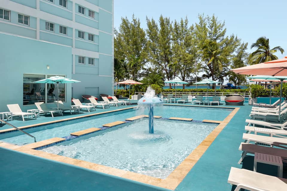Modern hotel pool with fountain, lounge chairs, umbrellas, and aqua-colored water