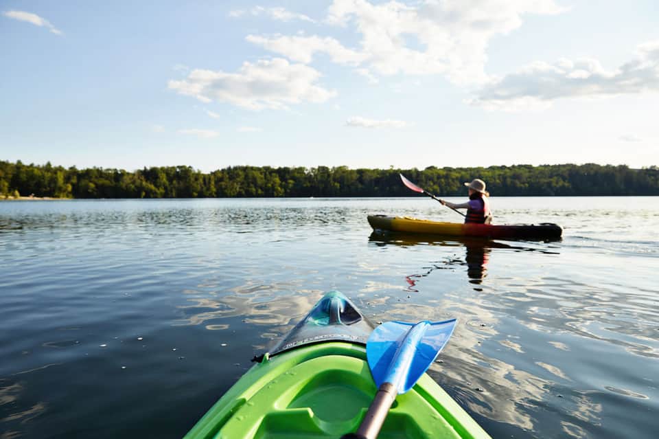 Two kayakers on calm lake with forested shoreline in background