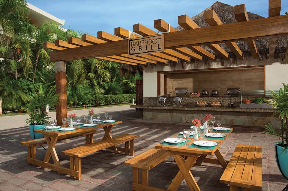 Barefoot Grill outdoor dining area with wooden tables, pergola, and built-in grill station