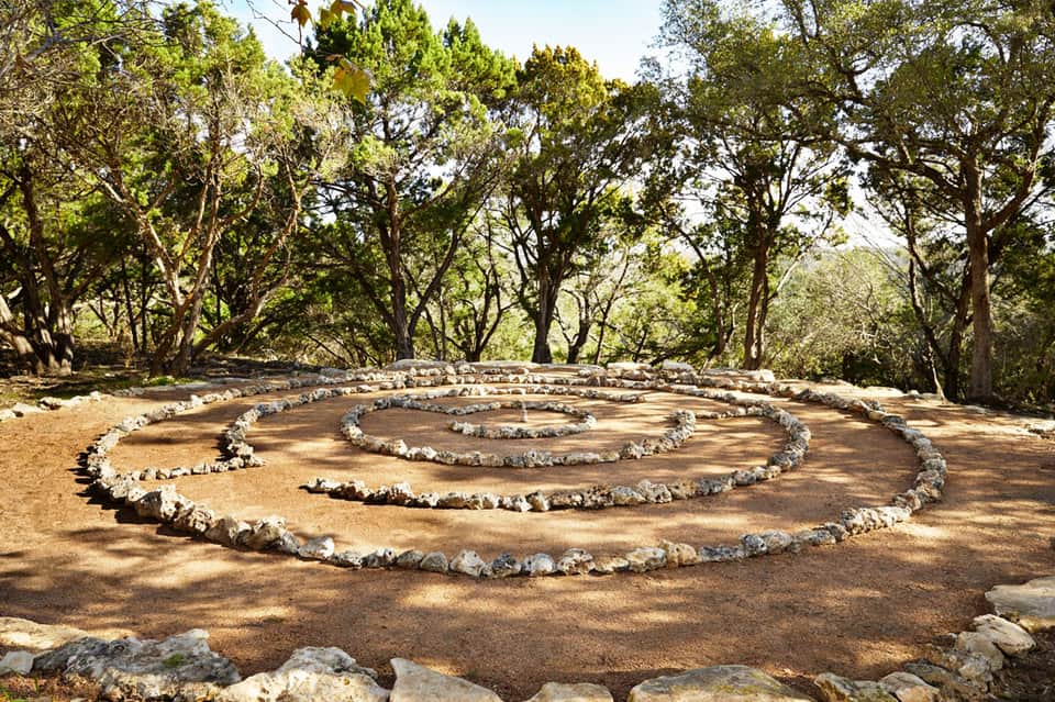 Spiral labyrinth pattern made of white stones on brown earth surrounded by tall trees