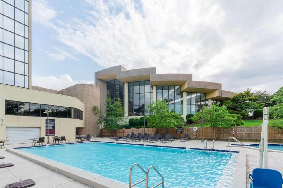 Resort outdoor pool with modern brick building and lounge chairs under cloudy sky