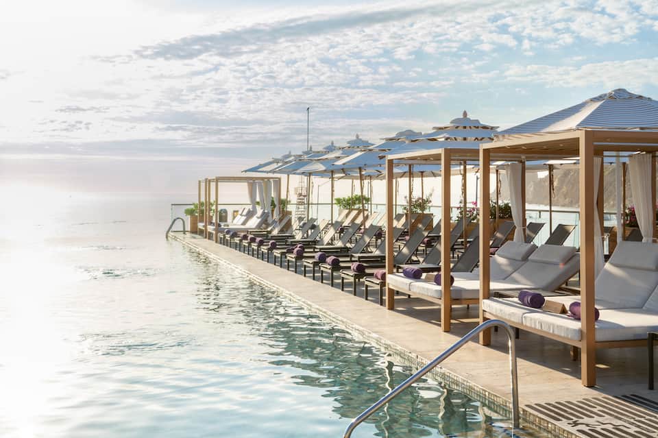 Luxury waterfront deck with wooden cabanas, lounge chairs, umbrellas overlooking calm ocean water