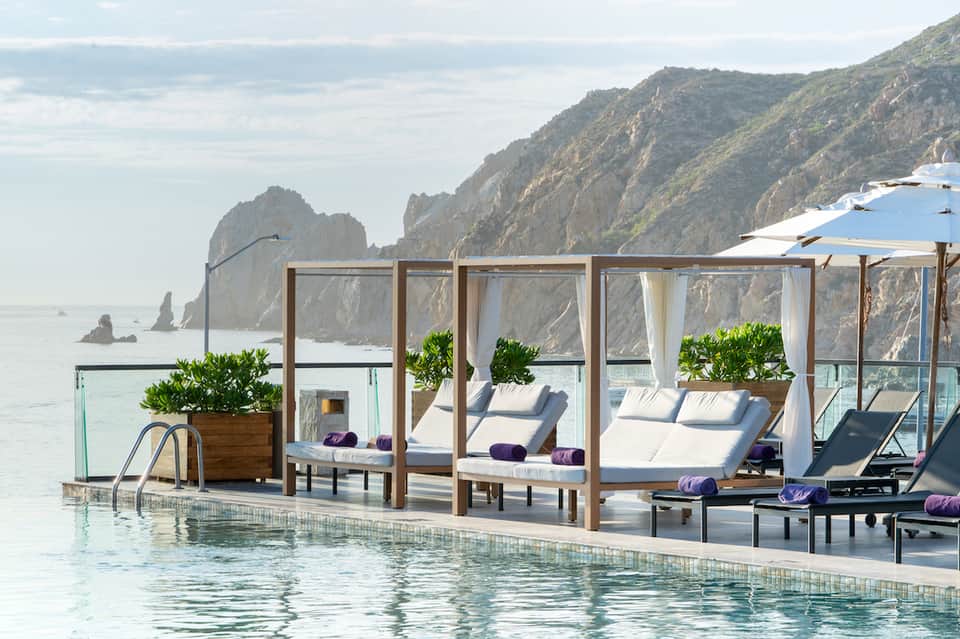 Oceanside pool cabanas with white curtains and loungers overlooking dramatic coastal cliffs