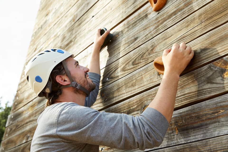 Man in white helmet rock climbing on wooden wall with handholds